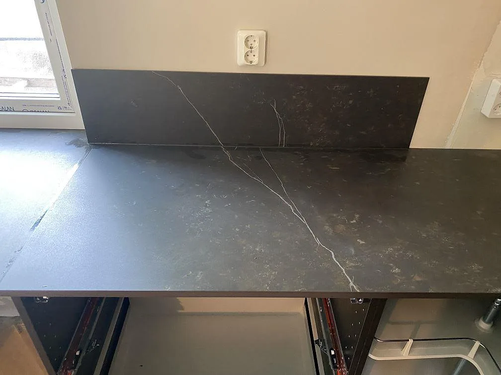 Matt Dekton Kelya bänkskiva med tydlig ljus ådring och uppvikt stänkkant längs väggen i ett kök i Genarp.