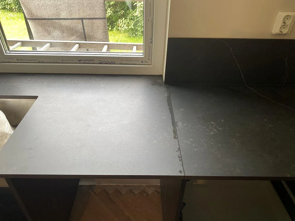 Mörk Dekton Kelya köksbänkskiva med stänkskydd vid fönstret i ett kök under inredning i Genarp.