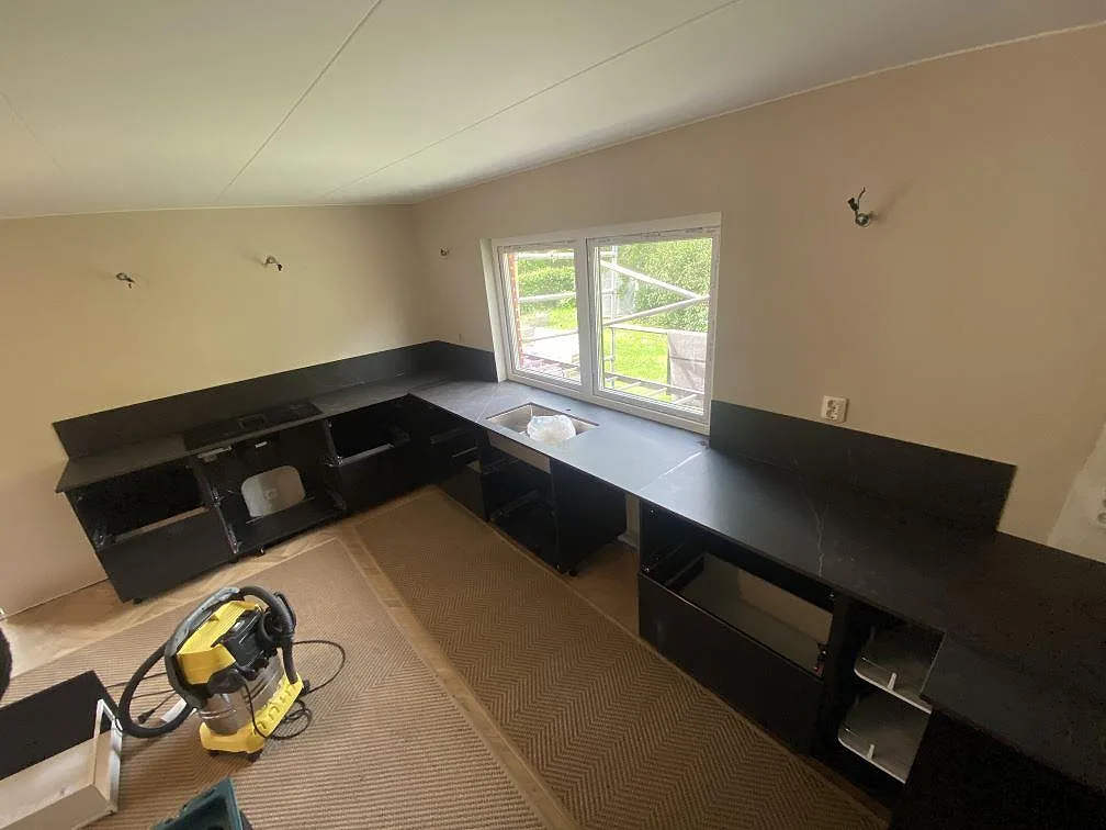 Översikt av ett vinkelkök med köksbänkskiva i mörk Dekton Kelya under montering i Genarp.