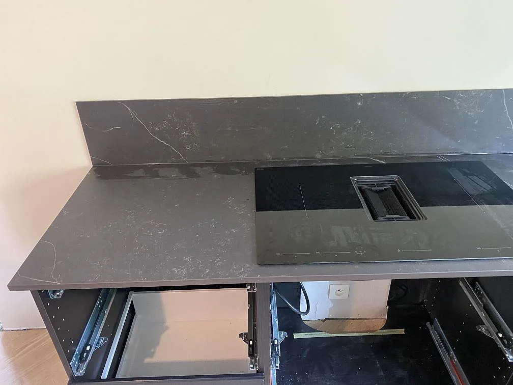 Mörk Dekton Kelya bänkskiva med infälld induktionshäll och uppvikt stänkskydd i samma sten i ett kök i Genarp.