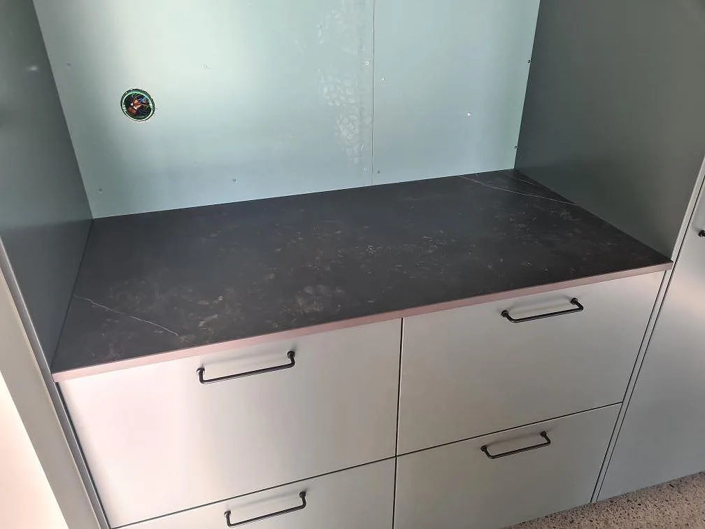 Installerad bänkskiva i matt Dekton Kelya keramik på vita lådor med mörka handtag i Glanshammar.