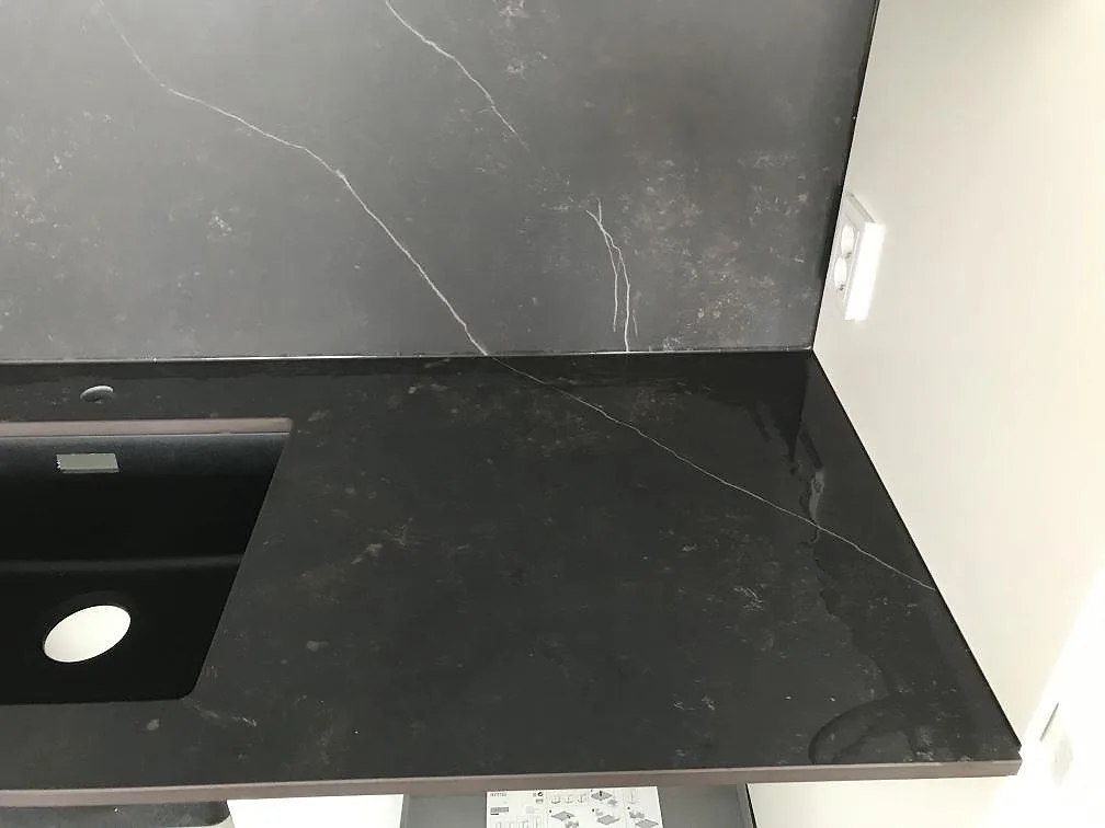 Mitterad gavel på köksö i Dekton Kelya där den vita ådringen löper ned över sidan, matt svart keramik i Göteborg.