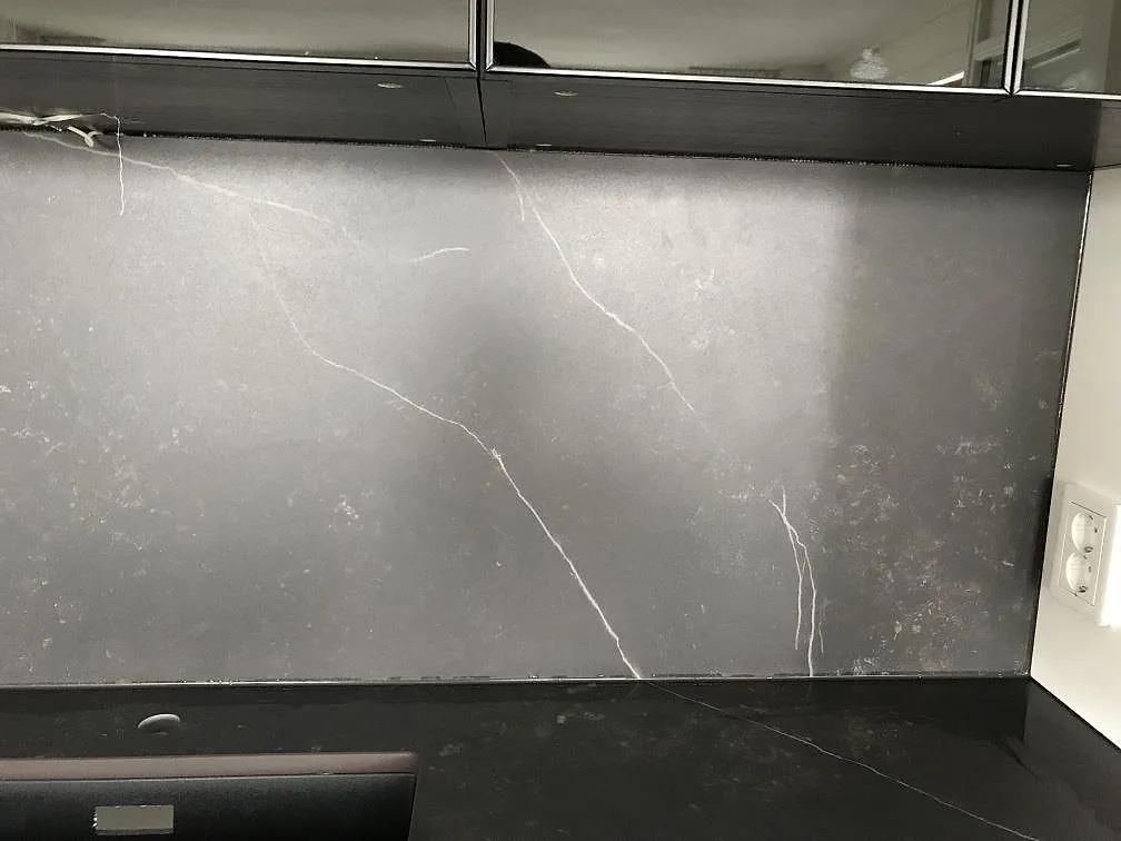 Heltäckande stänkskydd i Dekton Kelya, matt svart keramik med vit ådring, ovanför mörk bänkskiva i ett kök i Göteborg.
