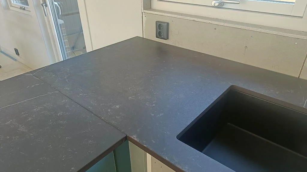 Hörn av Dekton Kelya bänkskiva med underlimmad mörk kompositho i ett kök i Hässleholm.