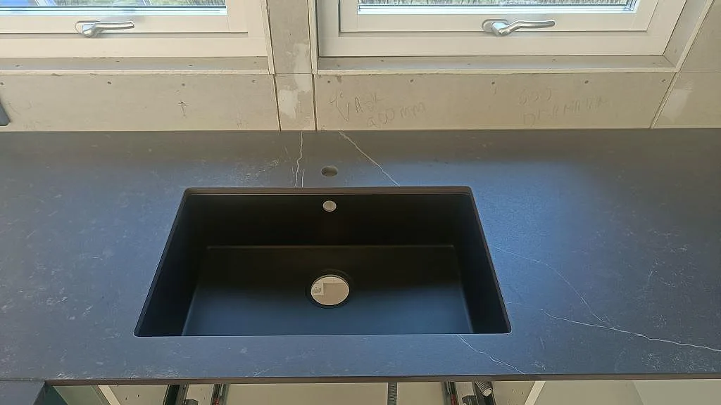 Underlimmad mörk kompositho i matt Dekton Kelya med ljus ådring i ett kök i Hässleholm.