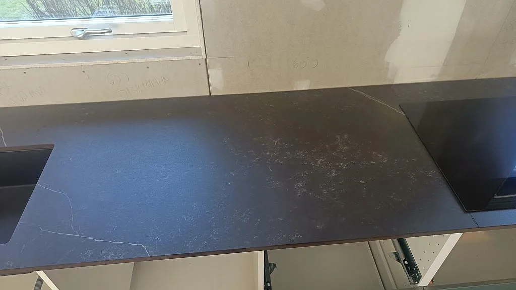 Bänkskiva i Dekton Kelya med induktionshäll och underlimmad ho längs en fönstervägg i ett kök i Hässleholm.