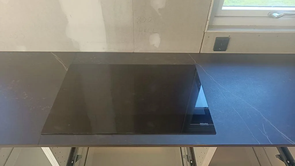 Induktionshäll placerad ovanpå en matt mörkgrå Dekton Kelya bänkskiva i ett kök i Hässleholm.