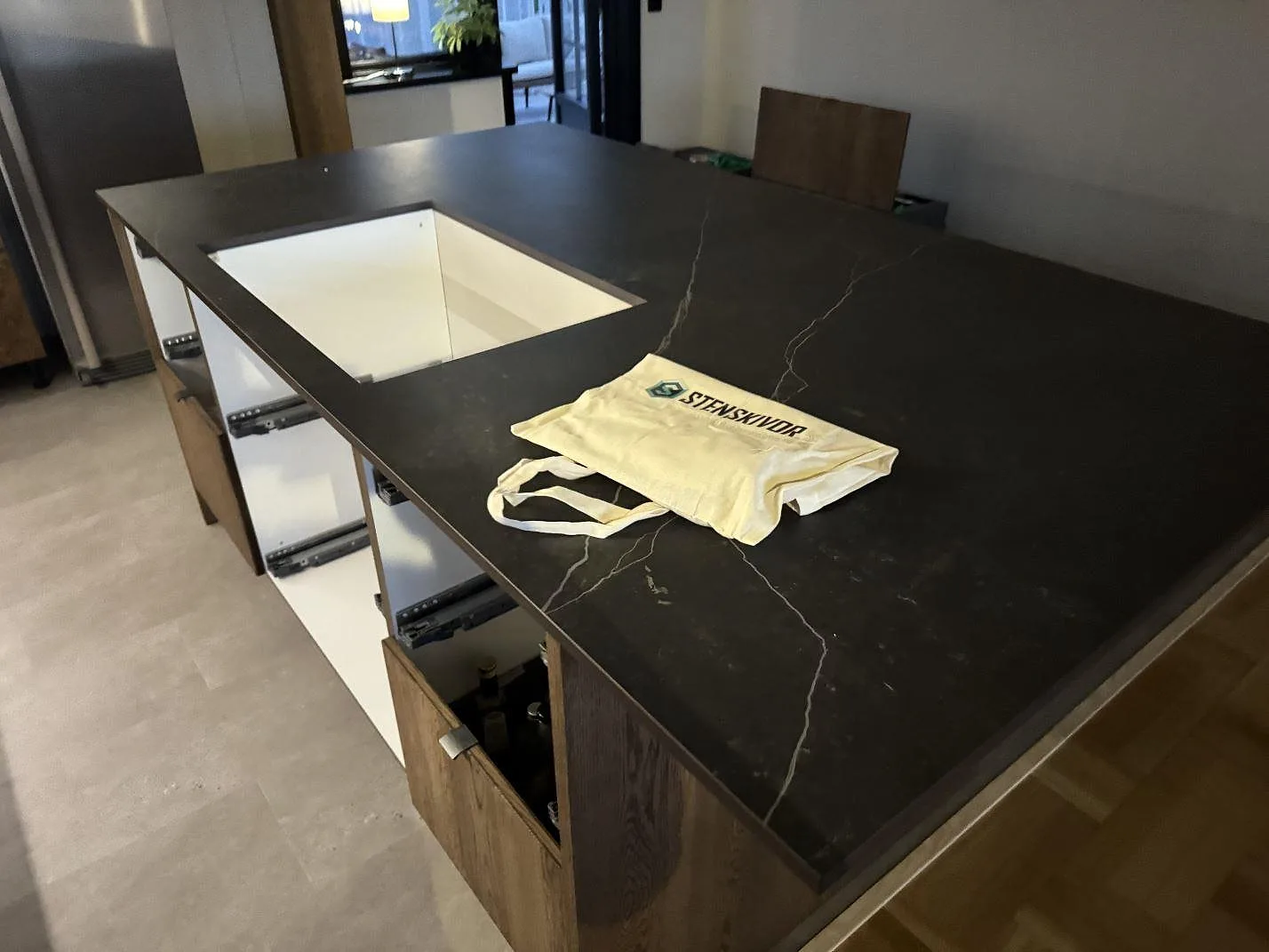 Köksö med bänkskiva i mörk matt Dekton Kelya keramik, synlig ådring och urtag i ett kök under montering i Halmstad.