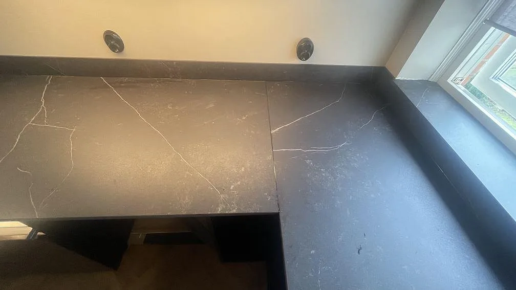 Matt bänkskiva i Dekton Kelya med uppvikt stänkkant och fönsterbänksdel längs fönstret i Helsingborg.