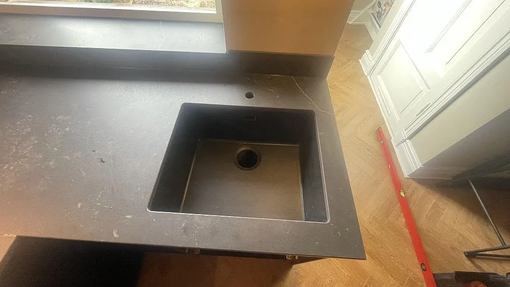 Närbild på diskhoöppning i matt Dekton Kelya med mörk köksbänkskiva och fönsterbänk i Helsingborg.