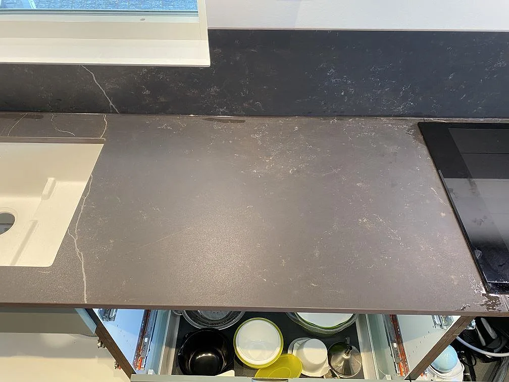 Vit underlimmad kompositdiskho i mörkgrå Dekton Kelya med uppvikt stänkkant under fönstret i ett kök i Höör.