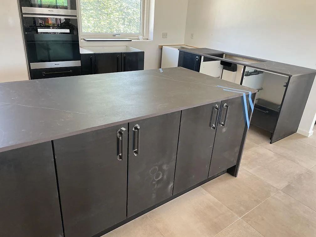 Matt köksbänkskiva i Dekton Kelya med stor köksö, mörkgrå skåp och väggbänk i ett kök i Hørsholm.