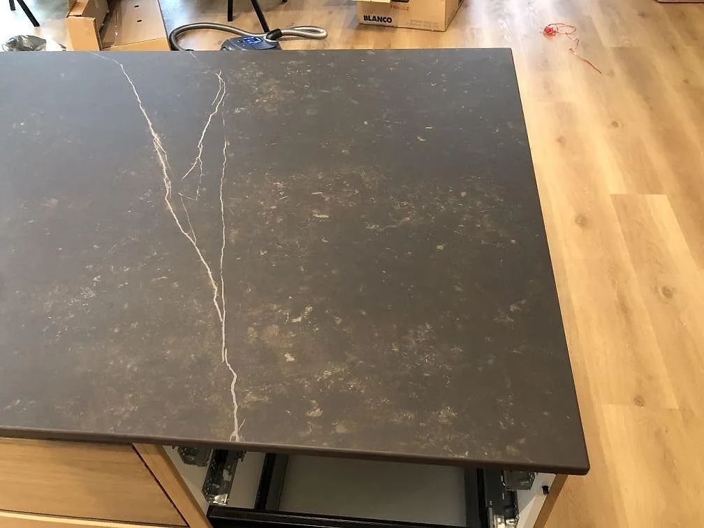 Köksö i Dekton Kelya med diskret ljus ådring och öppna lådstommar under montering i ett kök i Hvidovre.