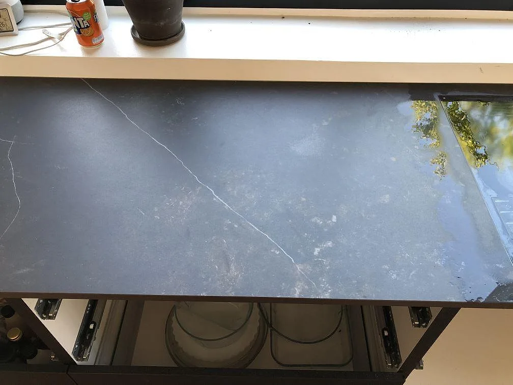 Bänkskiva i svart Dekton Kelya, matt keramik med ljusa ådror, längs köksfönstret i Jyderup.