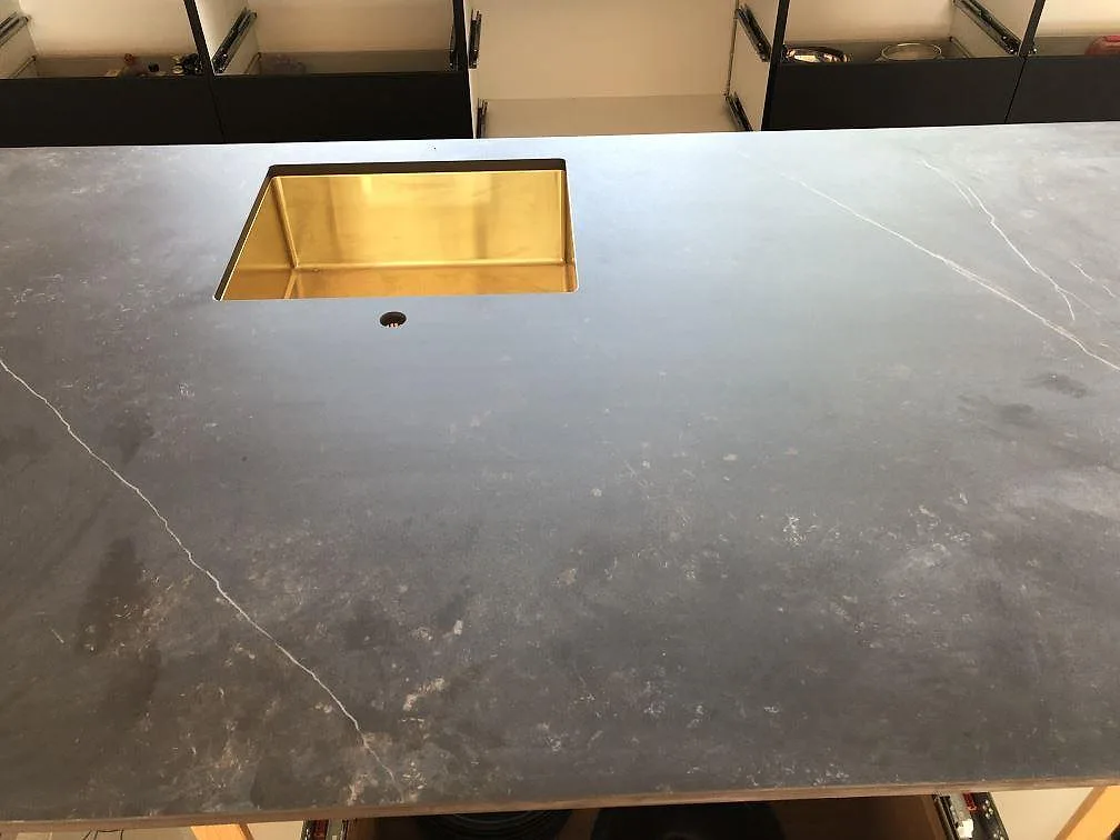 Underlimmad mässingsfärgad diskho i en köksö av svart Dekton Kelya, matt keramikbänkskiva i ett kök i Jyderup.
