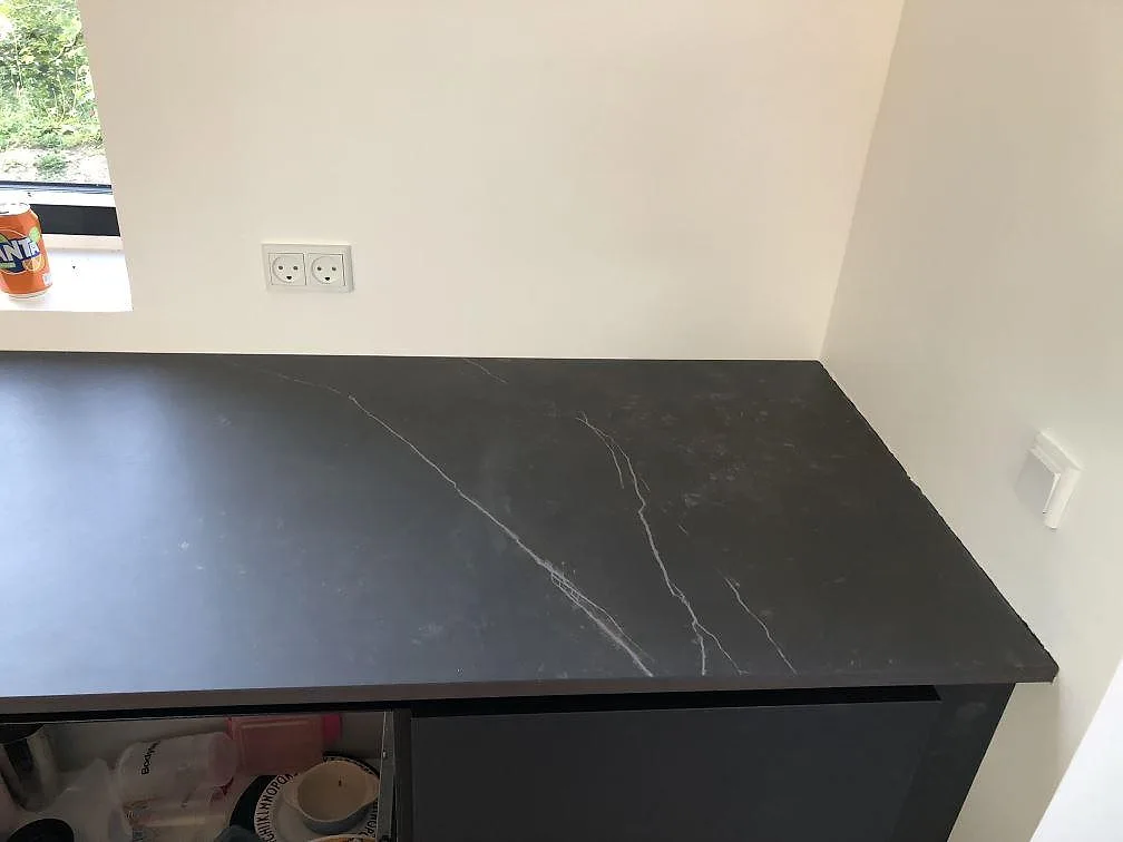 Köksbänkskiva i mörk Dekton Kelya med tydlig ljus ådring längs fönstret i ett kök i Jyderup.