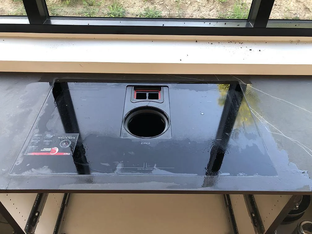 Bänkskiva i mörk Dekton Kelya med integrerad induktionshäll och downdraft-fläkt vid fönstret i ett kök i Jyderup.