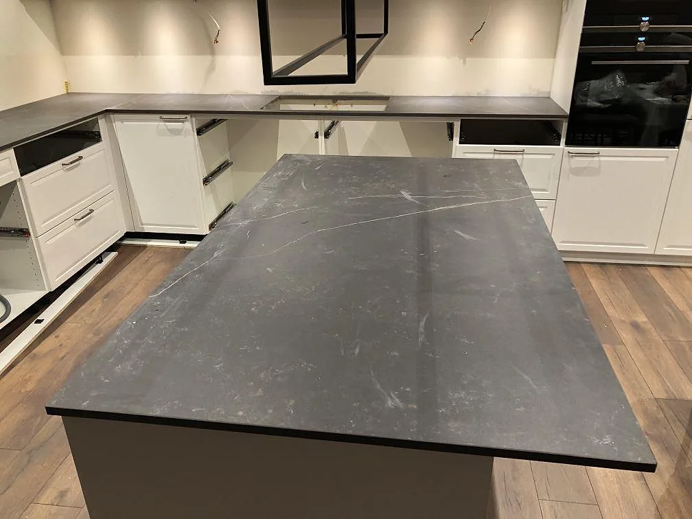 Köksbänkskiva och köksö i mörkgrå Dekton Kelya, matt, med ljusa ådror i ett kök i Kärna.