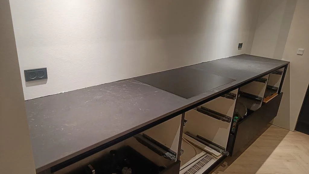 Köksbänkskiva i mörk Dekton Kelya keramik, matt, med infälld induktionshäll i en lång rad i ett kök under montering i Kolding.