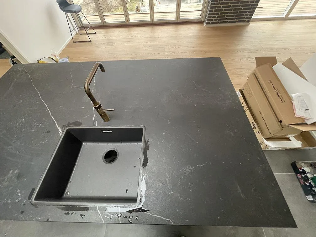 Köksbänkskiva och köksö i mörkgrå Dekton Kelya, matt, med underlimmad grå kompositdiskho och bronsfärgad blandare i ett kök i Kr.Hyllinge.