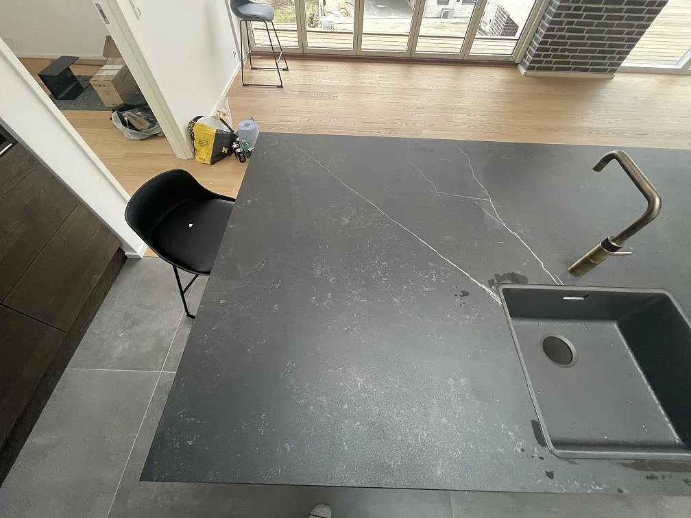 Köksö i mörkgrå Dekton Kelya med vit ådring och underlimmad kompositdiskho, fotad från sidan i ett kök i Kr.Hyllinge.