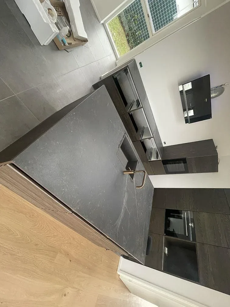 Köksö i Dekton Kelya med induktionshäll och bronsblandare i ett kök under montering i Kr.Hyllinge.