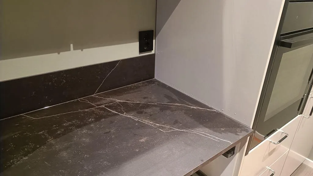 Detaljbild av matt Dekton Kelya som bänkskiva och lågt stänkskydd vid ugnsskåp i Kungsbacka.