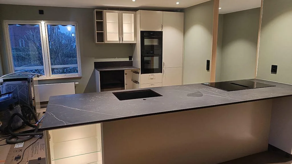 Köksbänkskiva i matt Dekton Kelya med mörk ådring, underlimmad svart diskho och häll i ett kök i Kungsbacka.