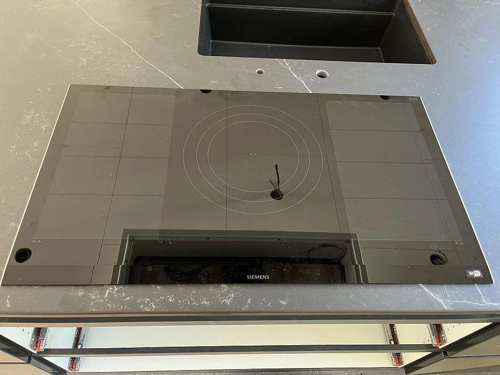 Siemens induktionshäll redo att sänkas ned i en köksö av matt grå Dekton Kelya intill diskhon i Löddeköpinge.