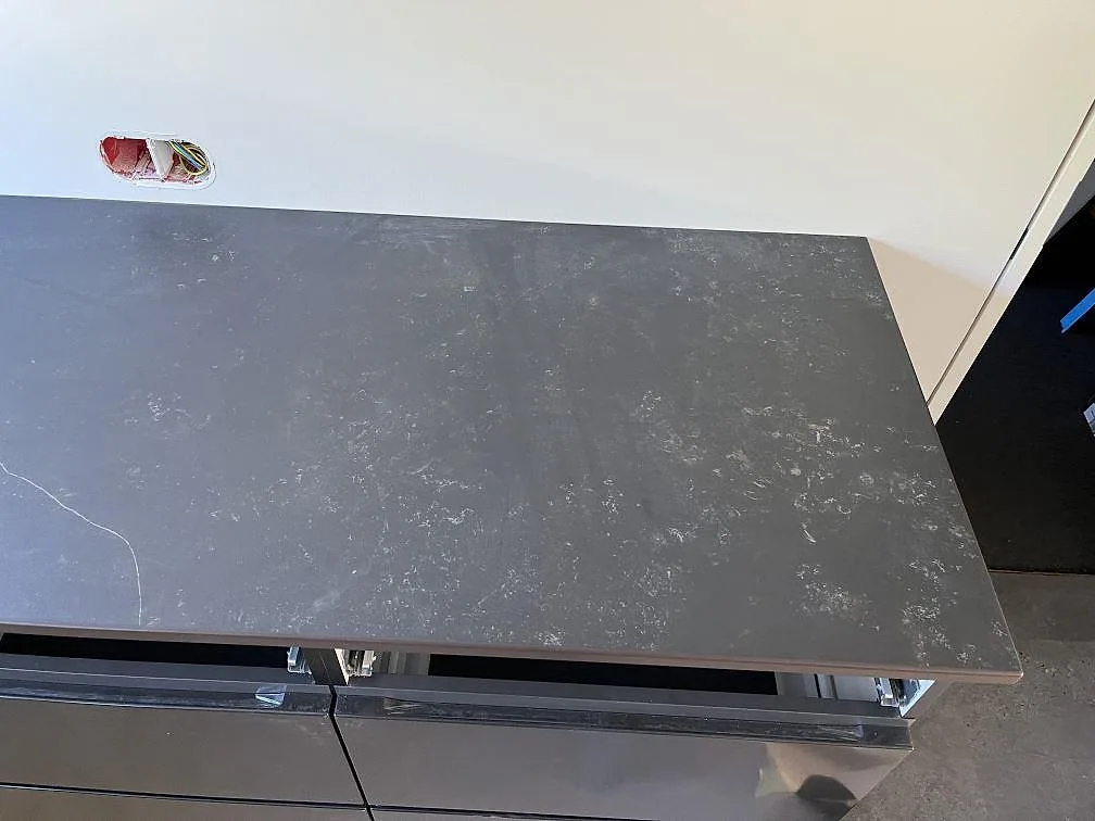 Köksbänkskiva i grå Dekton Kelya, matt keramik, monterad på köksö med öppna lådstommar under monteringen i Löddeköpinge.