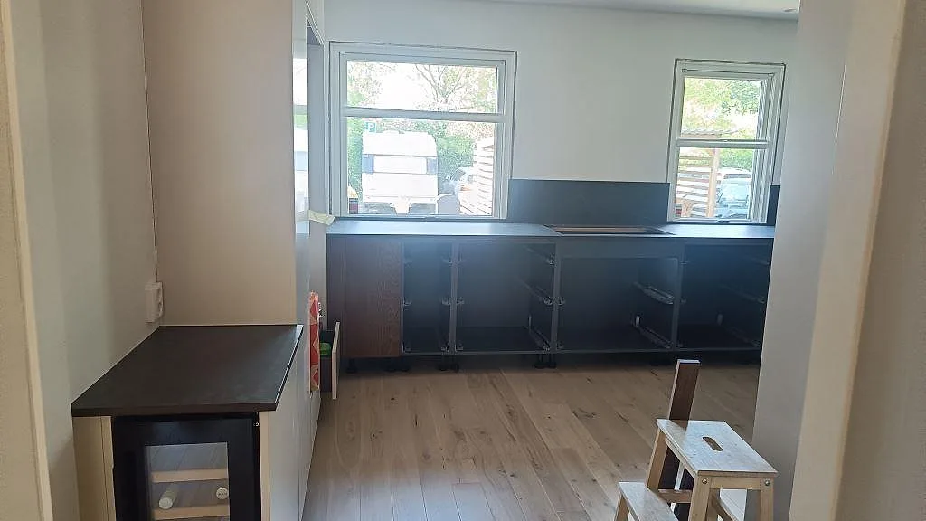 Köksbänkskiva i matt Dekton Kelya i ett kök i Lomma, med mörka skåpsstommar och lågt stänkskydd vid stora fönster.