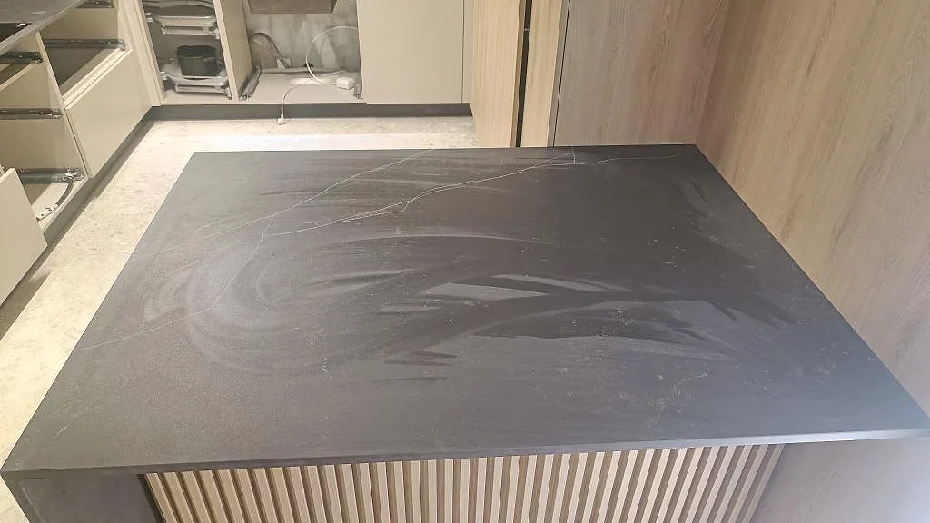Ovansida på stor köksö i matt Dekton Kelya med mörk ådrad yta under montering i Staffanstorp.