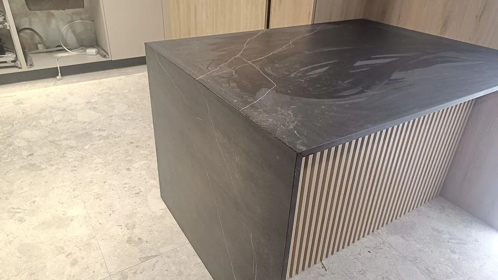 Detalj av köksö i matt Dekton Kelya med fallande sida, ljus ådring och ribbad träfront i Staffanstorp.