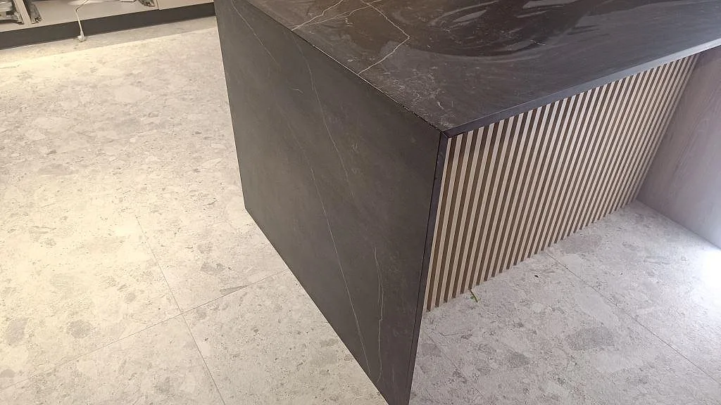 Närbild på fallande sida i matt Dekton Kelya och ribbad träfront på köksö i Staffanstorp.