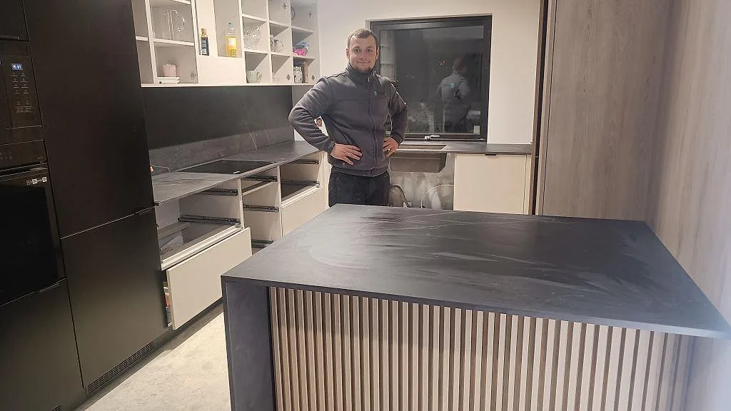 Köksö i matt Dekton Kelya med ribbad träfront och mörk köksbänkskiva under montering i Staffanstorp.