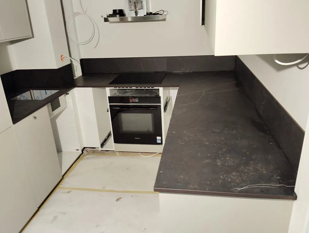 Köksbänkskiva i mörk matt Dekton Kelya med matchande stänkskydd i ett vitt kök under montering i Stockholm.