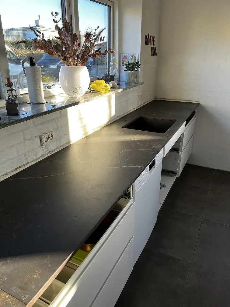 Köksbänkskiva i mörkgrå Dekton Kelya, matt, med underlimmad diskho längs en fönstervägg i ett kök i Taastrup.
