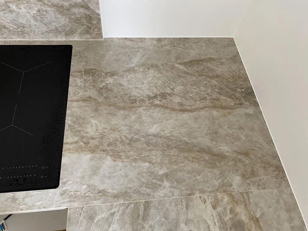 Arbetsyta i matt Dekton Kelya intill svart häll, med gråmarmorerad keramik i ett kök i Viby Sjælland.