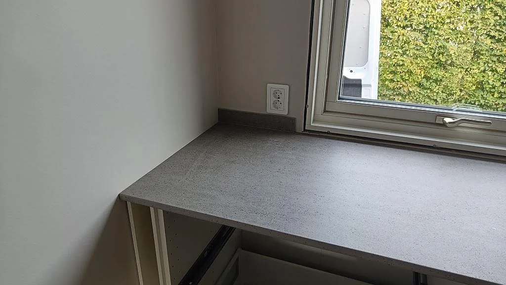 Matt Dekton Keon köksbänkskiva i keramik vid fönster med grå stenstruktur och låg stänkkant i Anderstorp.