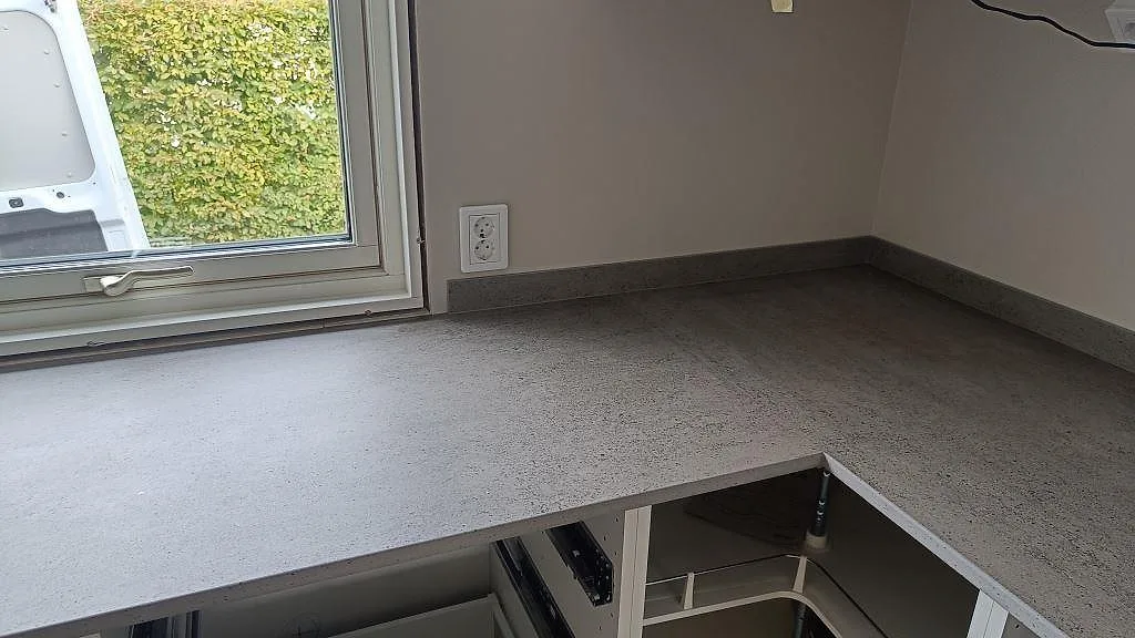 Närbild på matt Dekton Keon som köksbänkskiva i keramik med stänkkant och hörn runt fönstret i Anderstorp.