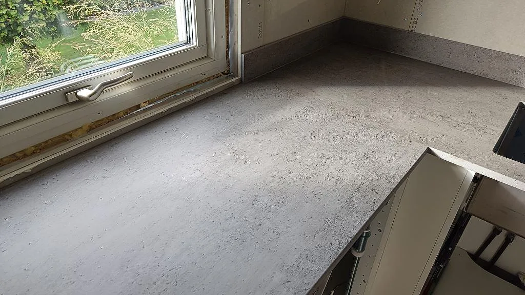 Köksbänkskiva i matt Dekton Keon keramik runt fönsterhörnet med grå yta och kort stänkkant i Anderstorp.