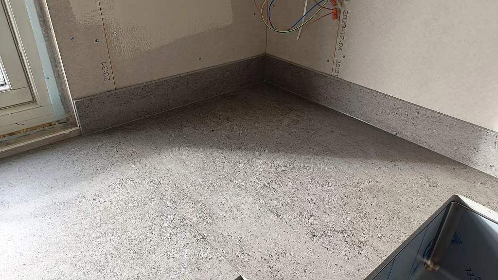 Detalj av grå Dekton Keon bänkskiva i matt keramik med stänkkant och synlig monteringsvägg i köket i Anderstorp.