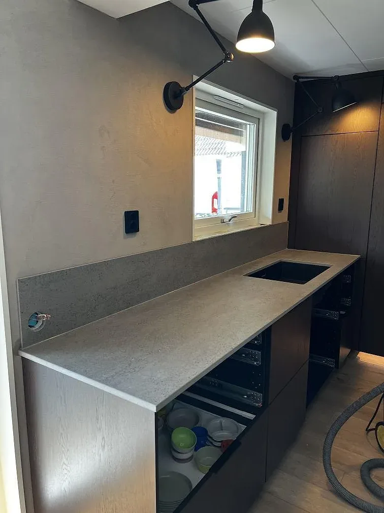 Matt köksbänkskiva i Dekton Keon med halvö, träinredning och stora fönster under montering i Falkenberg.