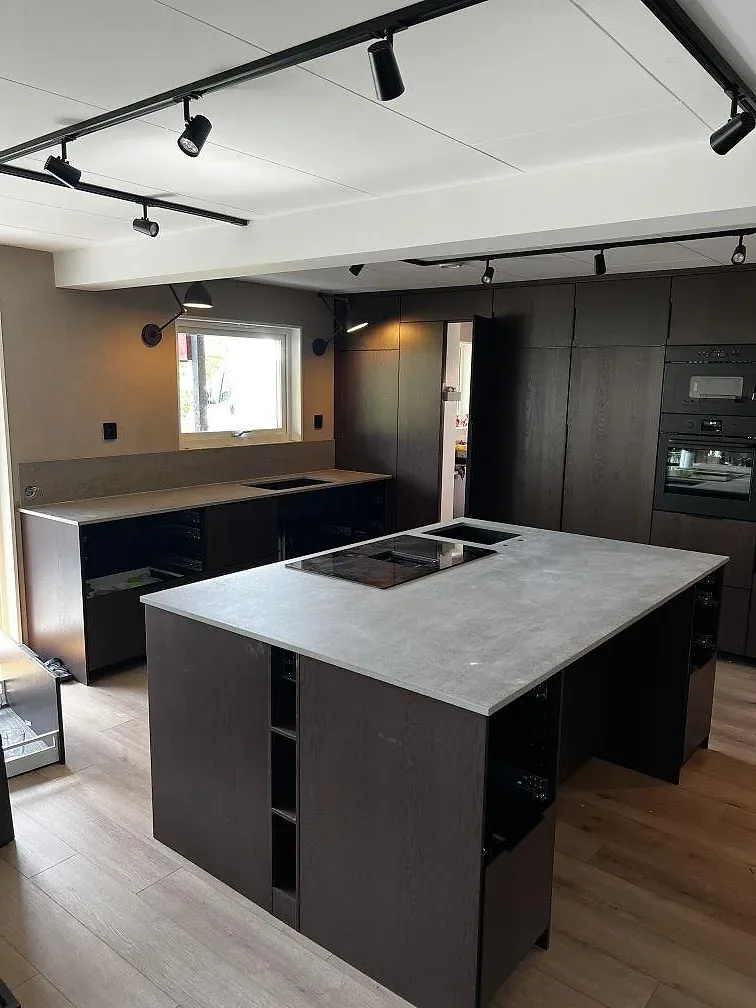 Köksbänkskiva i matt Dekton Keon, grå keramik, på en halvö med svart häll i ett kök i Falkenberg.