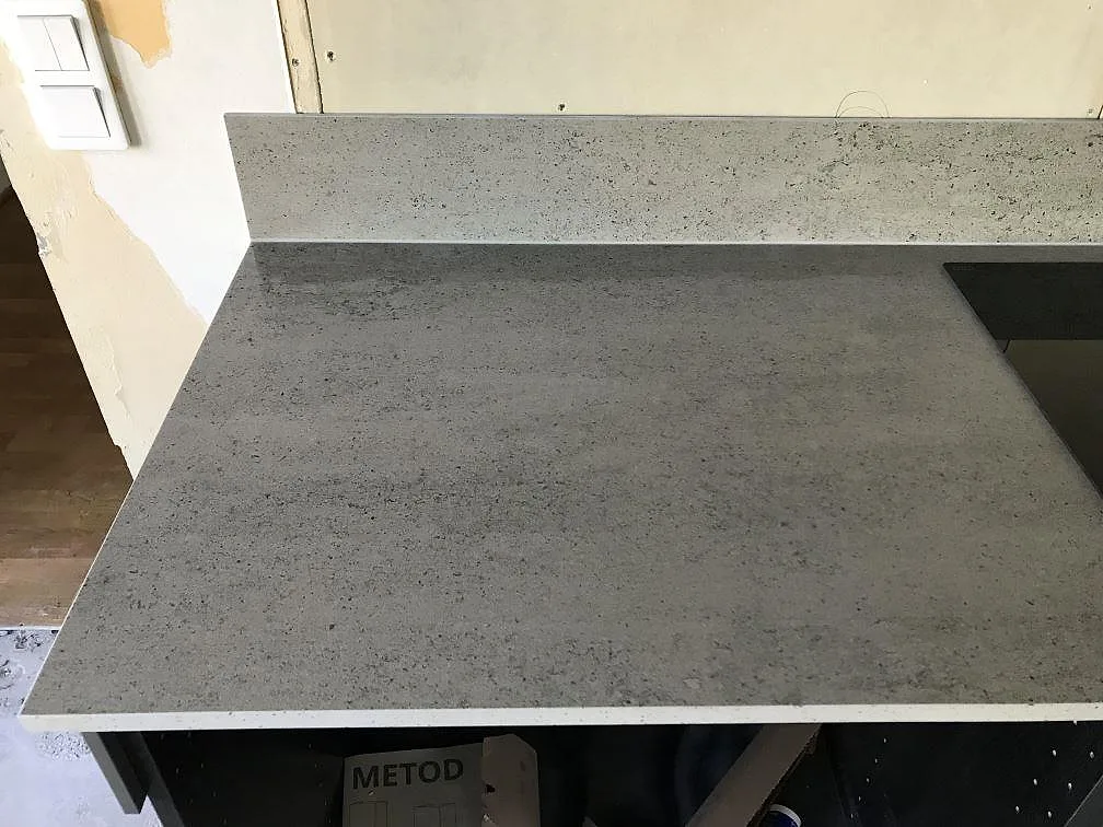 Köksbänkskiva i matt Dekton Keon med uppvikt stänkkant och cementlookens fina struktur i ett kök i Höviksnäs.