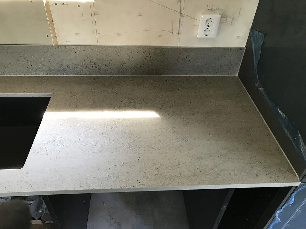 Underlimmad mörk kompositdiskho i en köksbänkskiva av Dekton Keon med uppvikt stänkskydd och eluttag i ett kök i Höviksnäs.