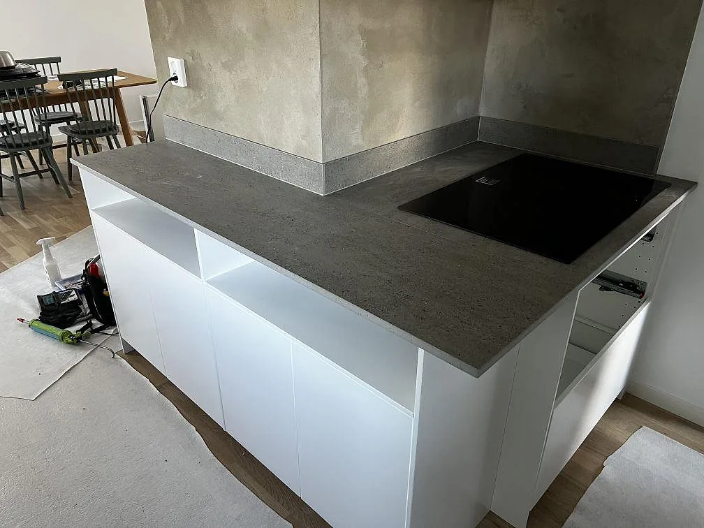 Dekton Keon köksbänkskiva i matt keramik med halvö, svart häll och uppvikt stänkskydd under montering i Kalmar.