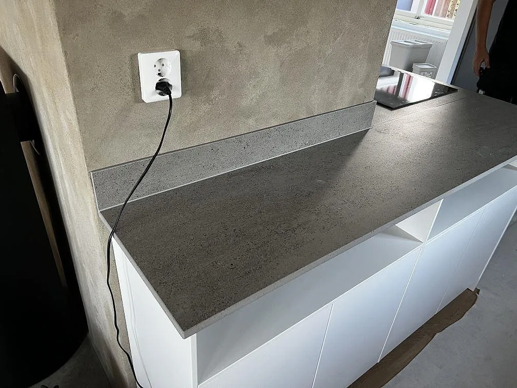 Lång arbetsyta i matt Dekton Keon keramik med stänkskydd och vit köksstomme under montering i Kalmar.