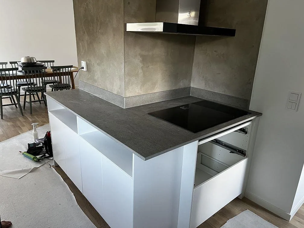 Matt köksbänkskiva i Dekton Keon keramik på en halvö med svart induktionshäll och grå väggbeklädnad i Kalmar.
