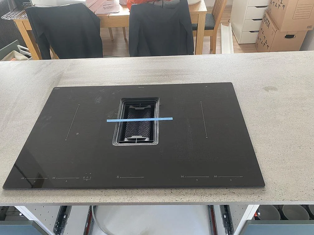 Induktionshäll placerad på en grå matt Dekton Keon köksbänkskiva under montering i ett kök i Klagstorp.
